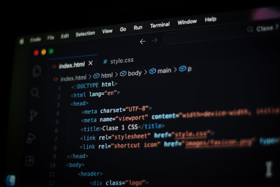 A close-up of a person's hand wearing a wristwatch, typing on a silver laptop with a black keyboard, placed on a wooden surface. The laptop screen displays lines of colorful code, indicating programmi